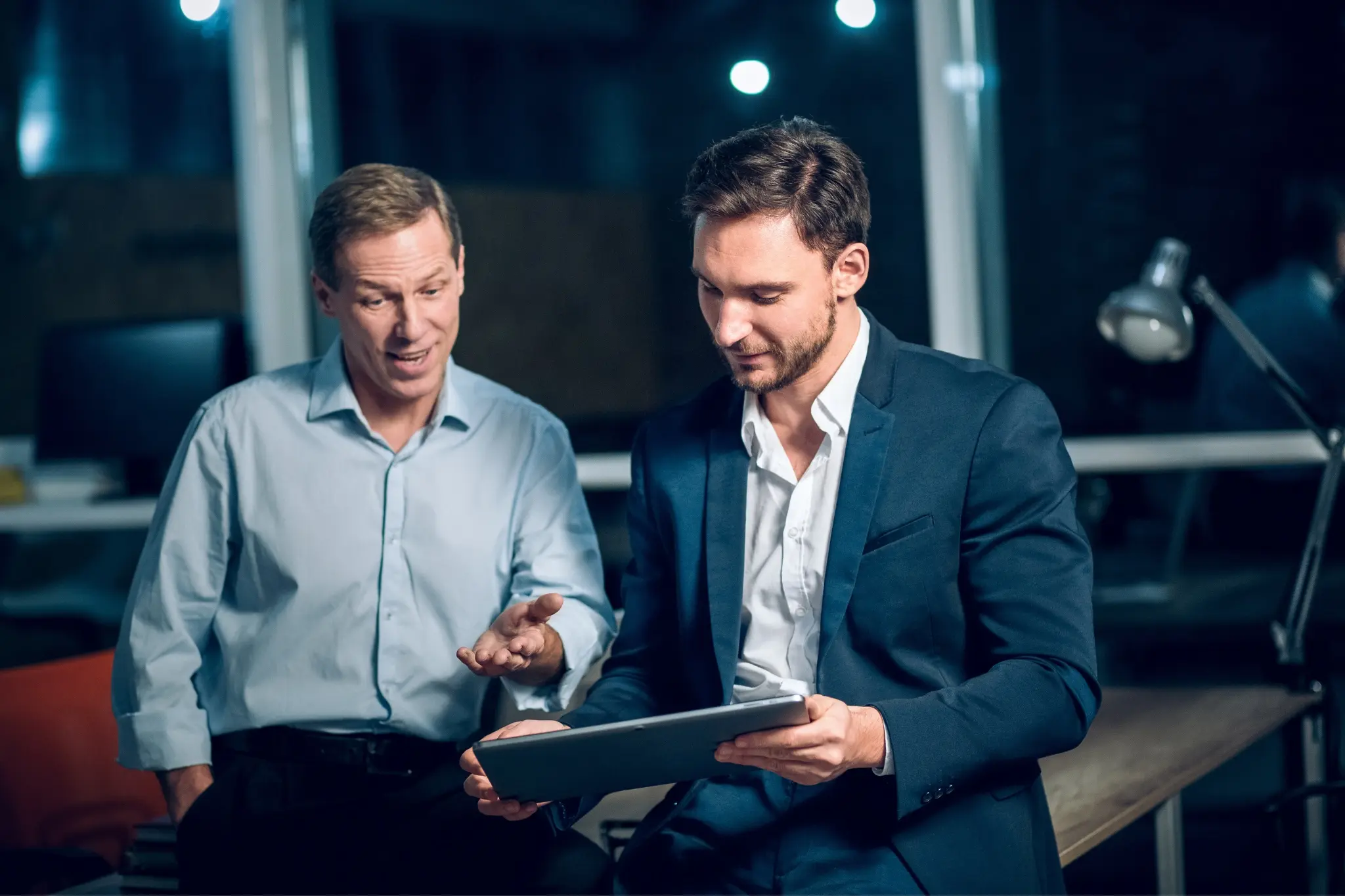 Two advisors discussing figures on a tablet during an evening strategy session